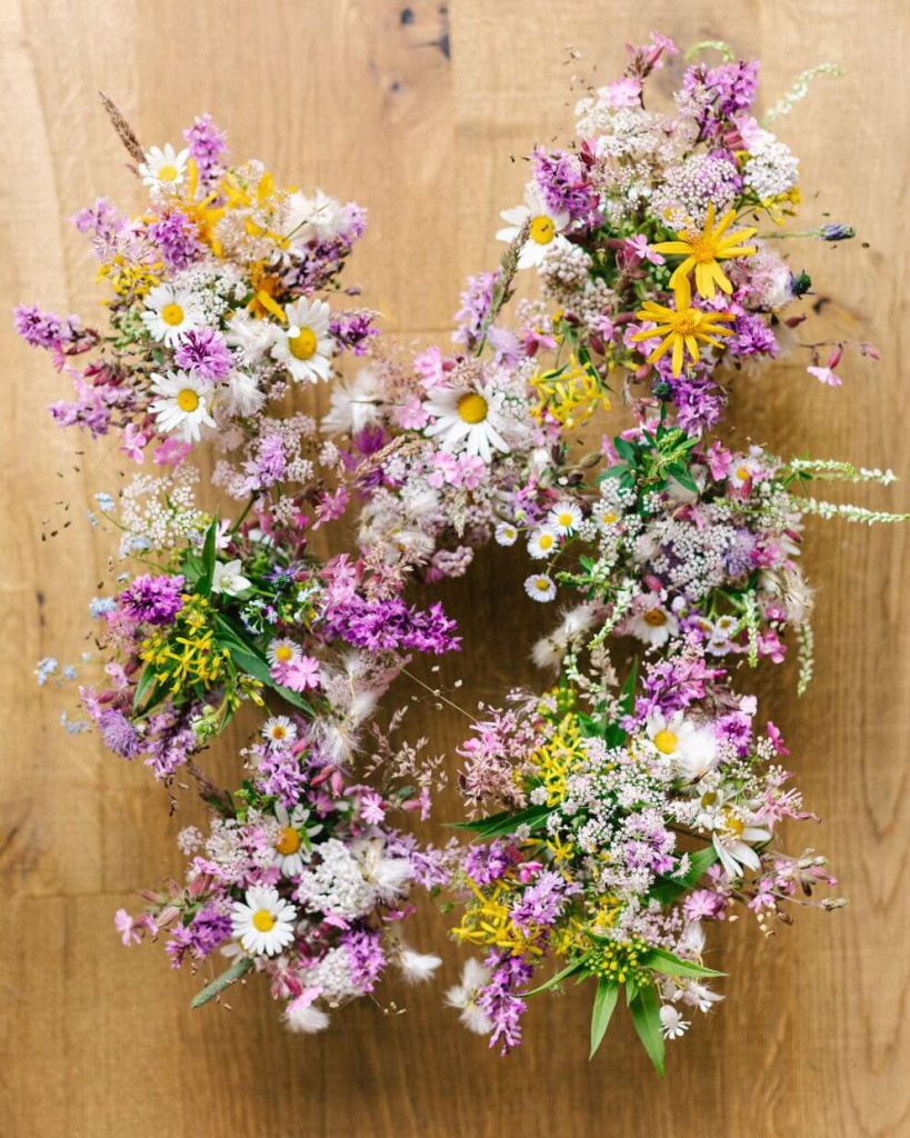 Bunte Frühlingsblumen in einem kranzförmigen Arrangement auf Holzuntergrund.