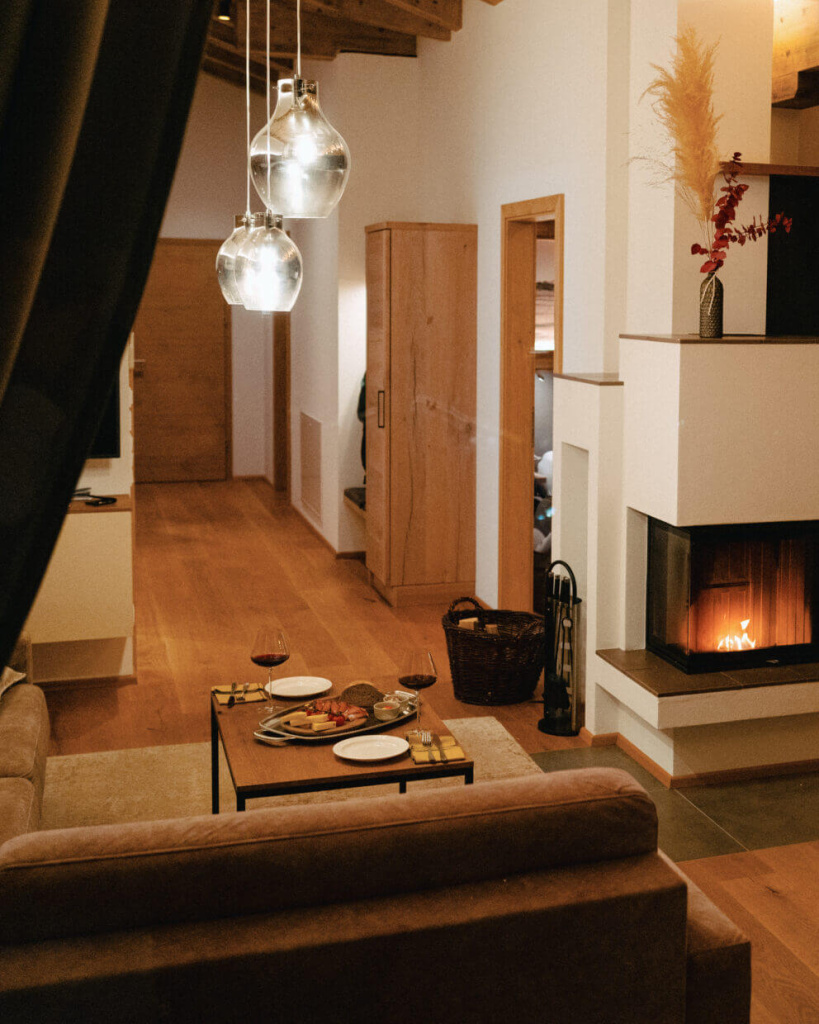 Stimmungsvolle Wohnatmosphäre mit bequemer Couch, offenem Kamin und gedecktem Tisch.