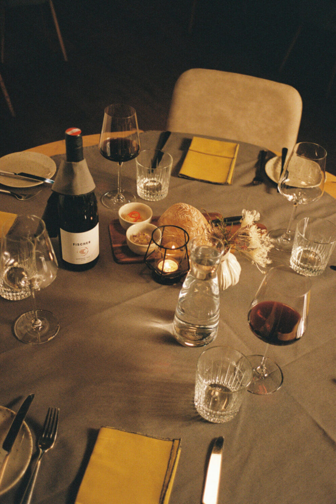Elegant gedeckter Tisch mit Wein, Wasser, Geschirr und dekorativen Elementen.
